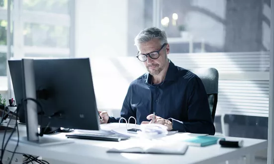 Mann sitzt an seinem Schreibtisch und überprüft Finanzdokumente im Büro, um Financial Compliance zu gewährleisten.